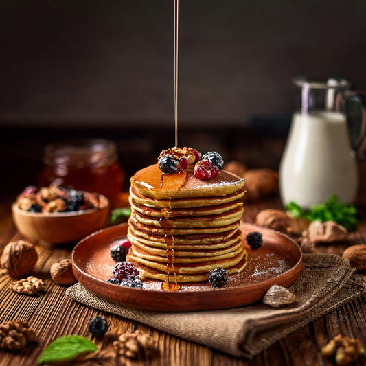 Pancakes mit Beeren, Nüssen und Ahornsirup, daneben ein Glas Milch